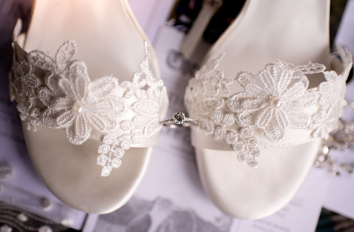 Delicate white lace bridal flats with floral embellishments photographed in soft lighting.