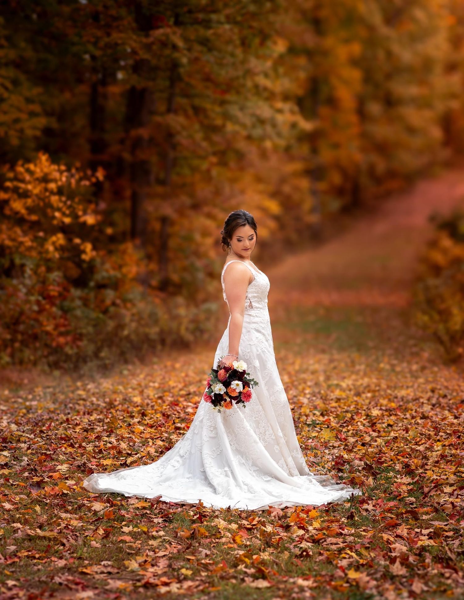 A bride in a white lace dress holding a bouquet amid vibrant autumn foliage.