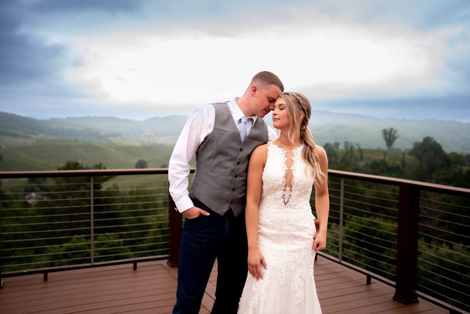 Newlyweds share an intimate moment on a deck overlooking rolling hills and mountains.