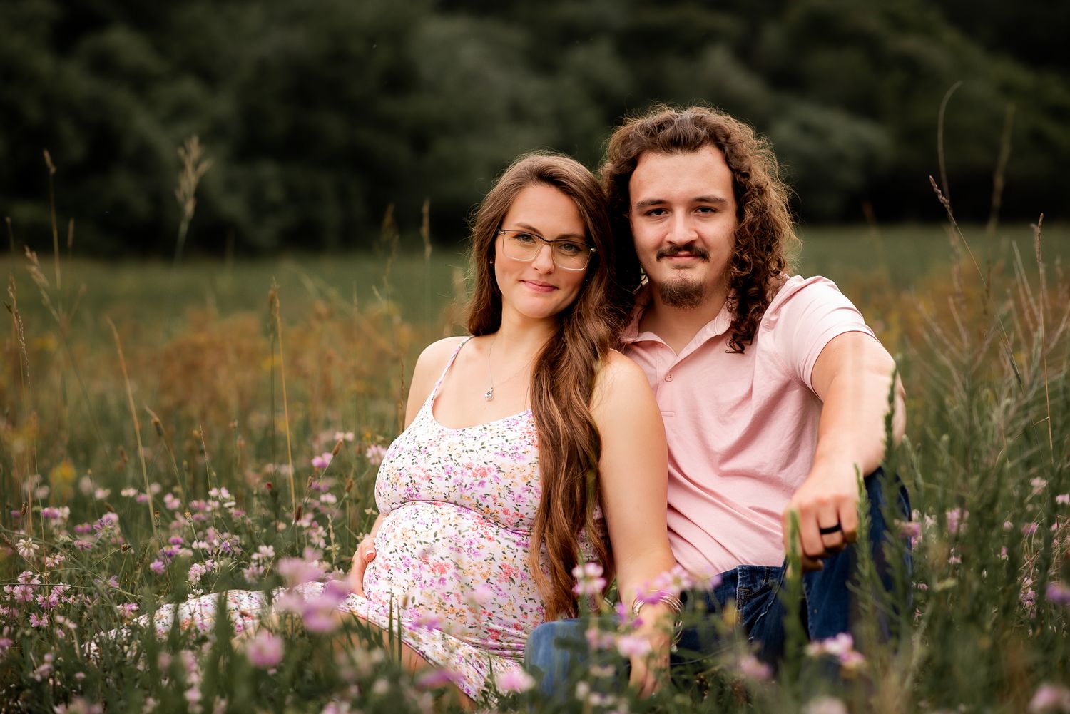 A couple sits together in a wildflower meadow during a summer evening photoshoot.