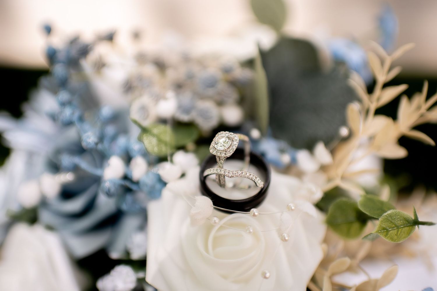 Wedding rings styled among soft blue and white floral arrangements with greenery.