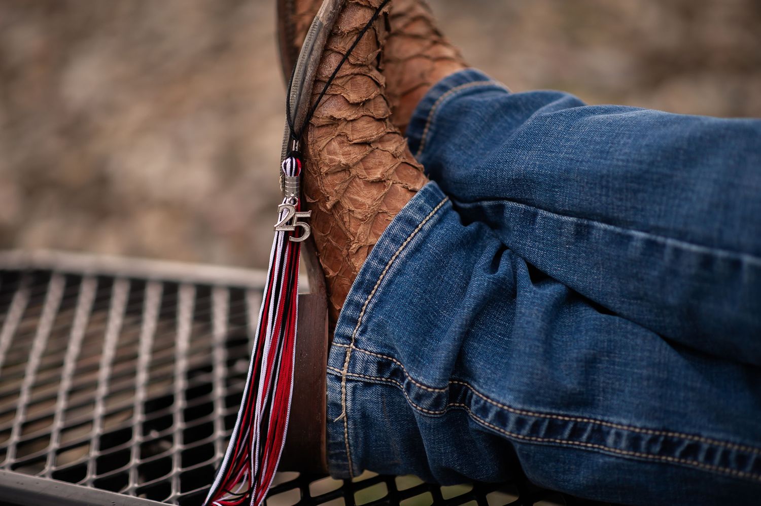 Close-up detail shot of brown leather boots and denim jeans with graduation tassel.