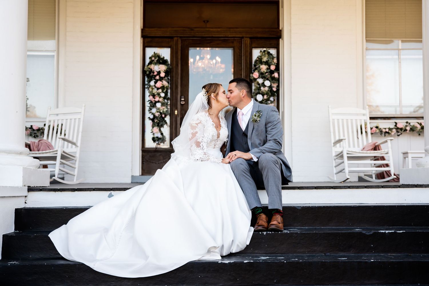 Wedding couple sitting together on rustic white porch with elegant decor.