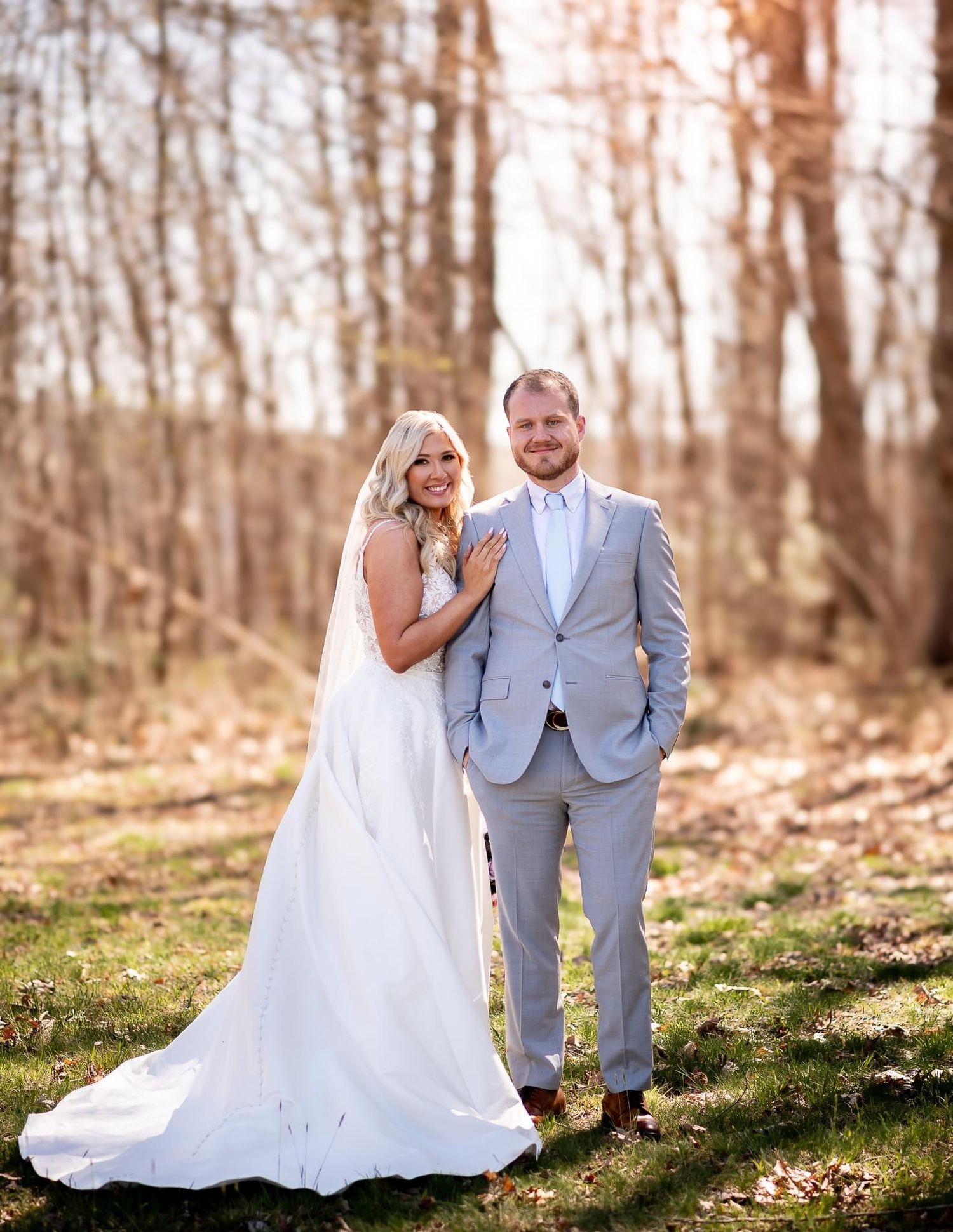 A couple in wedding attire poses in a sunlit autumn forest setting.
