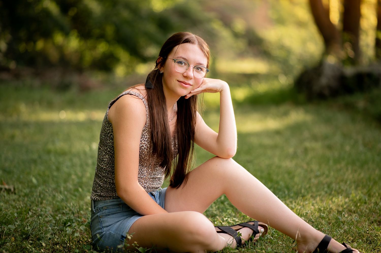 A natural outdoor portrait of someone sitting on grass in casual summer attire.