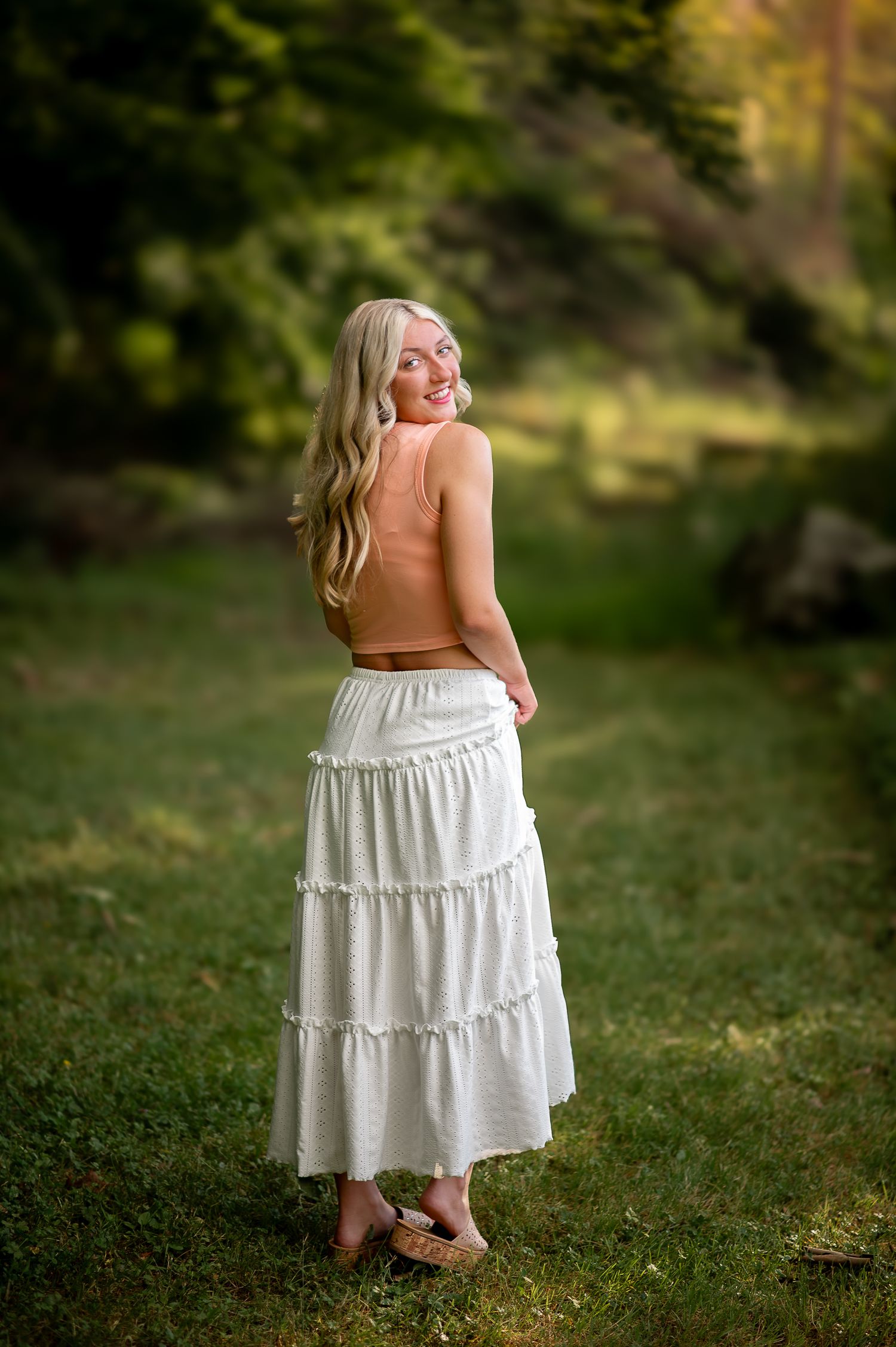 Summer portrait in white tiered maxi skirt looking over shoulder in garden setting.