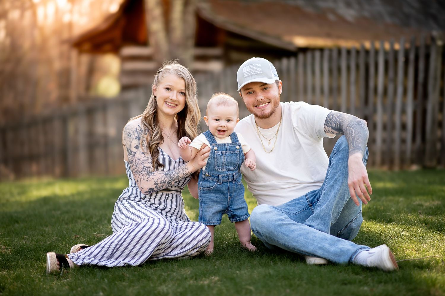 Family portrait on grass with rustic barn backdrop featuring casual denim and stripe outfit coordination.