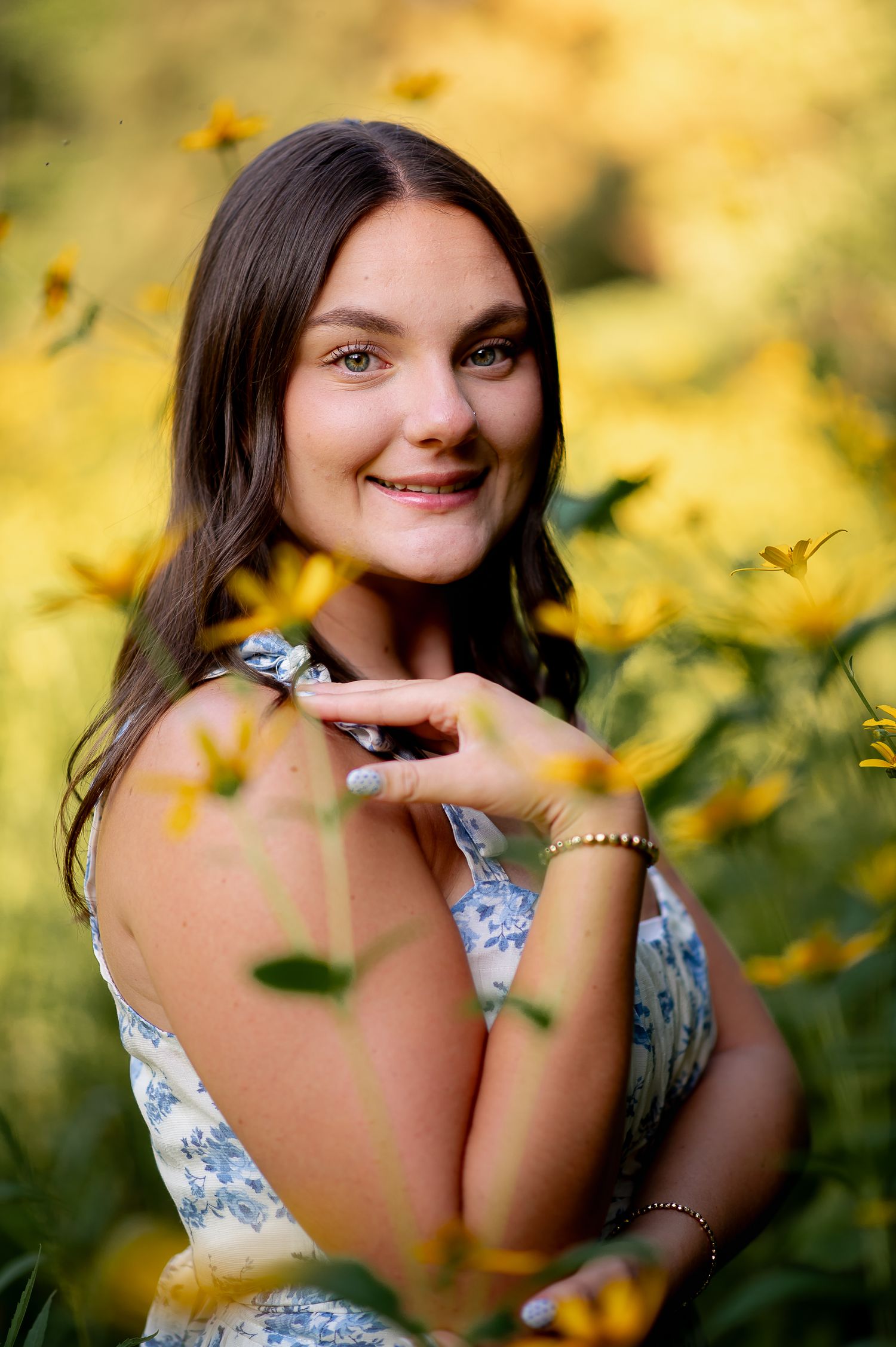Portrait of a woman in a floral dress smiling among yellow flowers with a soft bokeh background in summer light.