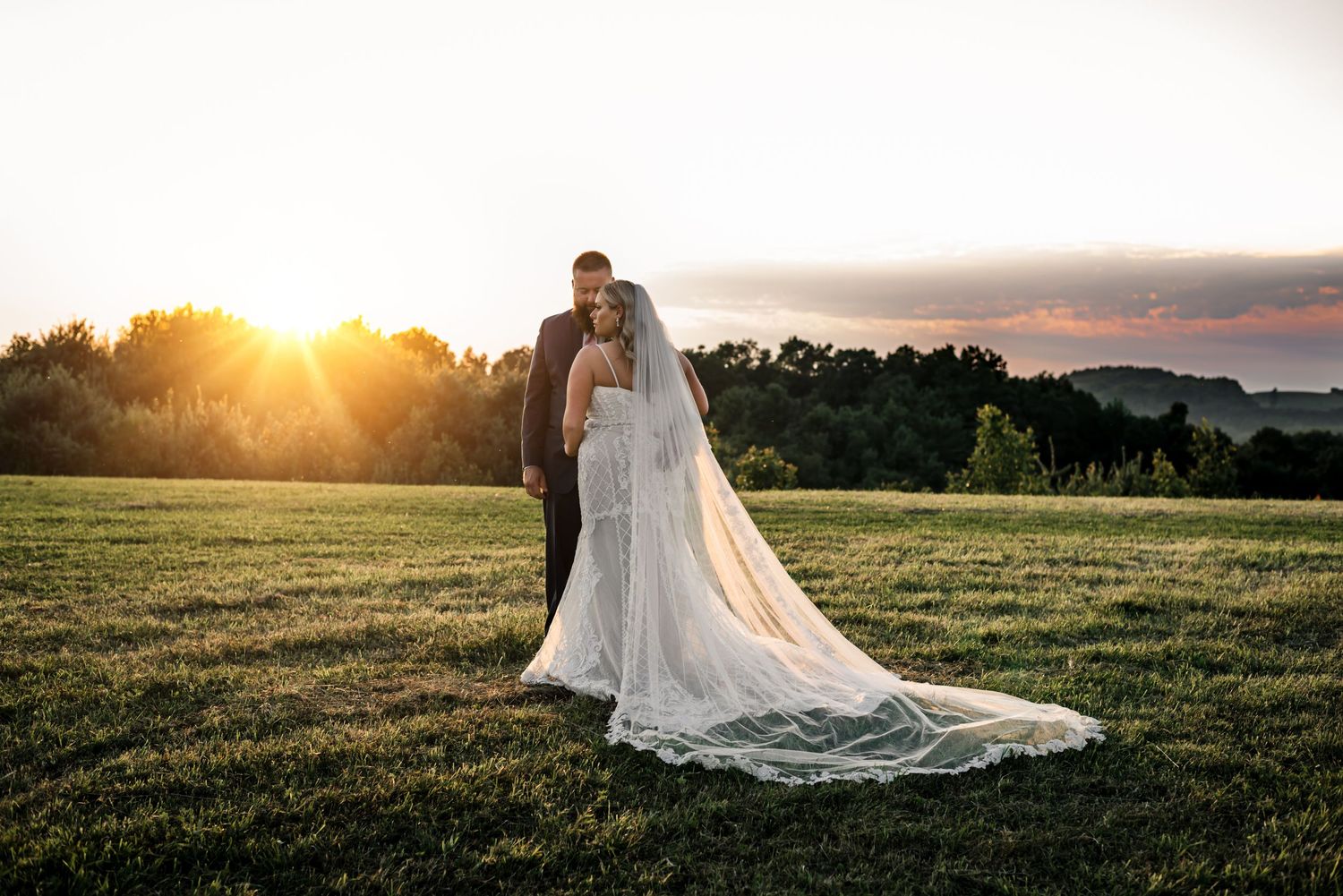 Wedding couple poses in golden sunset light across a serene field landscape.