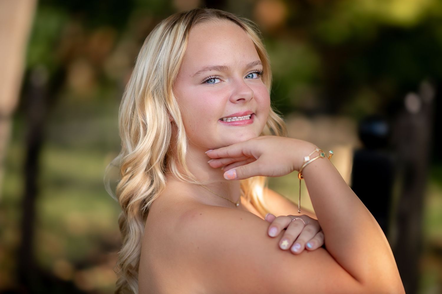 An outdoor portrait of a person with blonde hair resting their chin on their hand in natural sunlight.