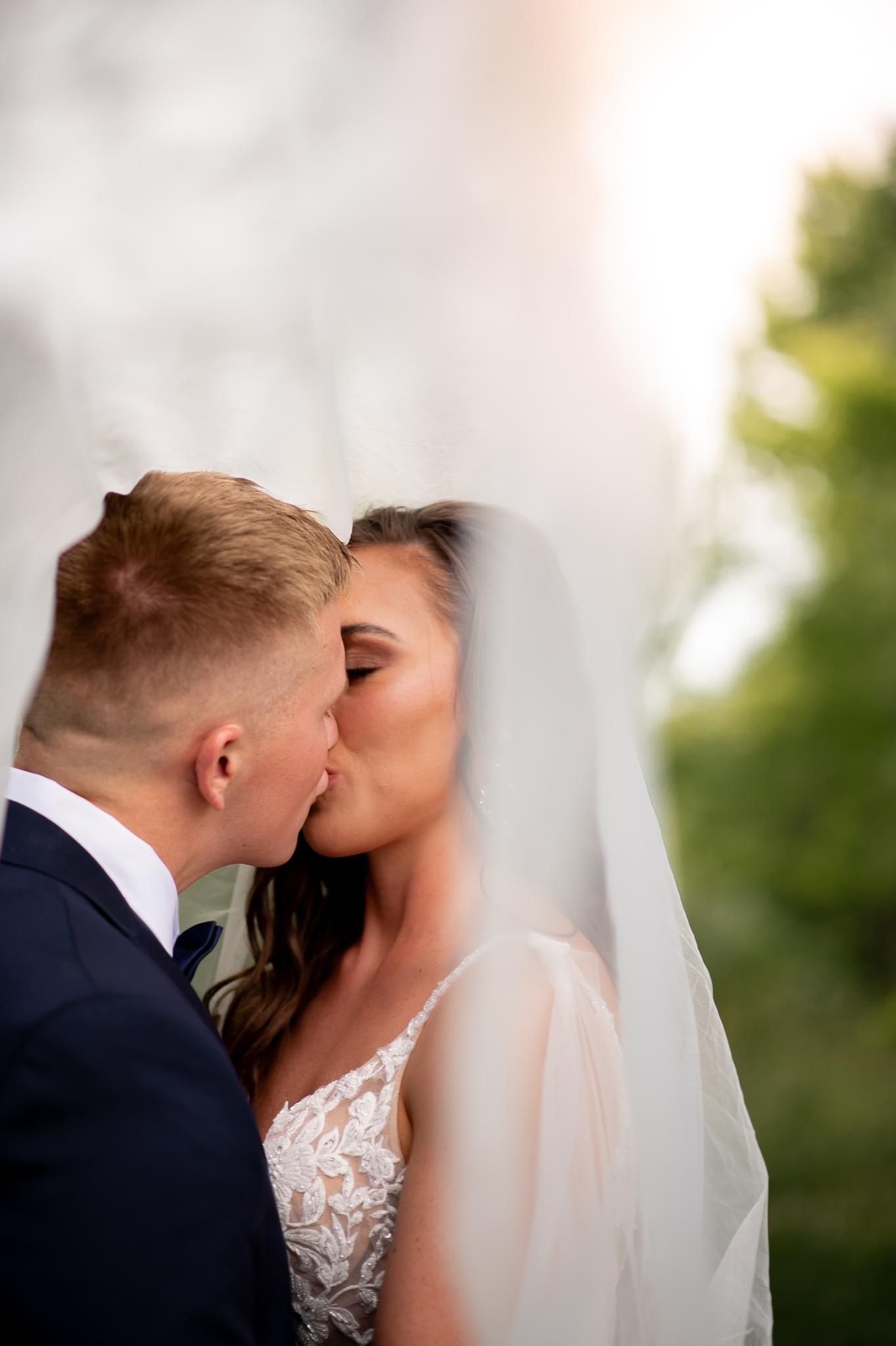 Intimate wedding moment captured under flowing veil during outdoor ceremony.