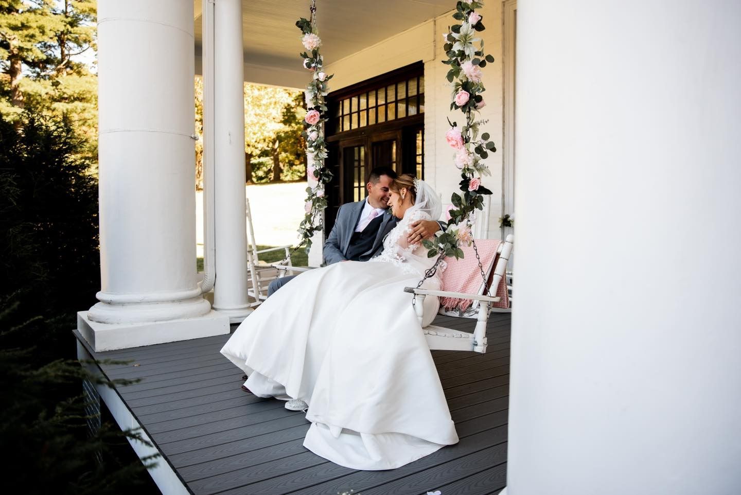 A couple shares a romantic moment on an elegant white porch with classical columns.