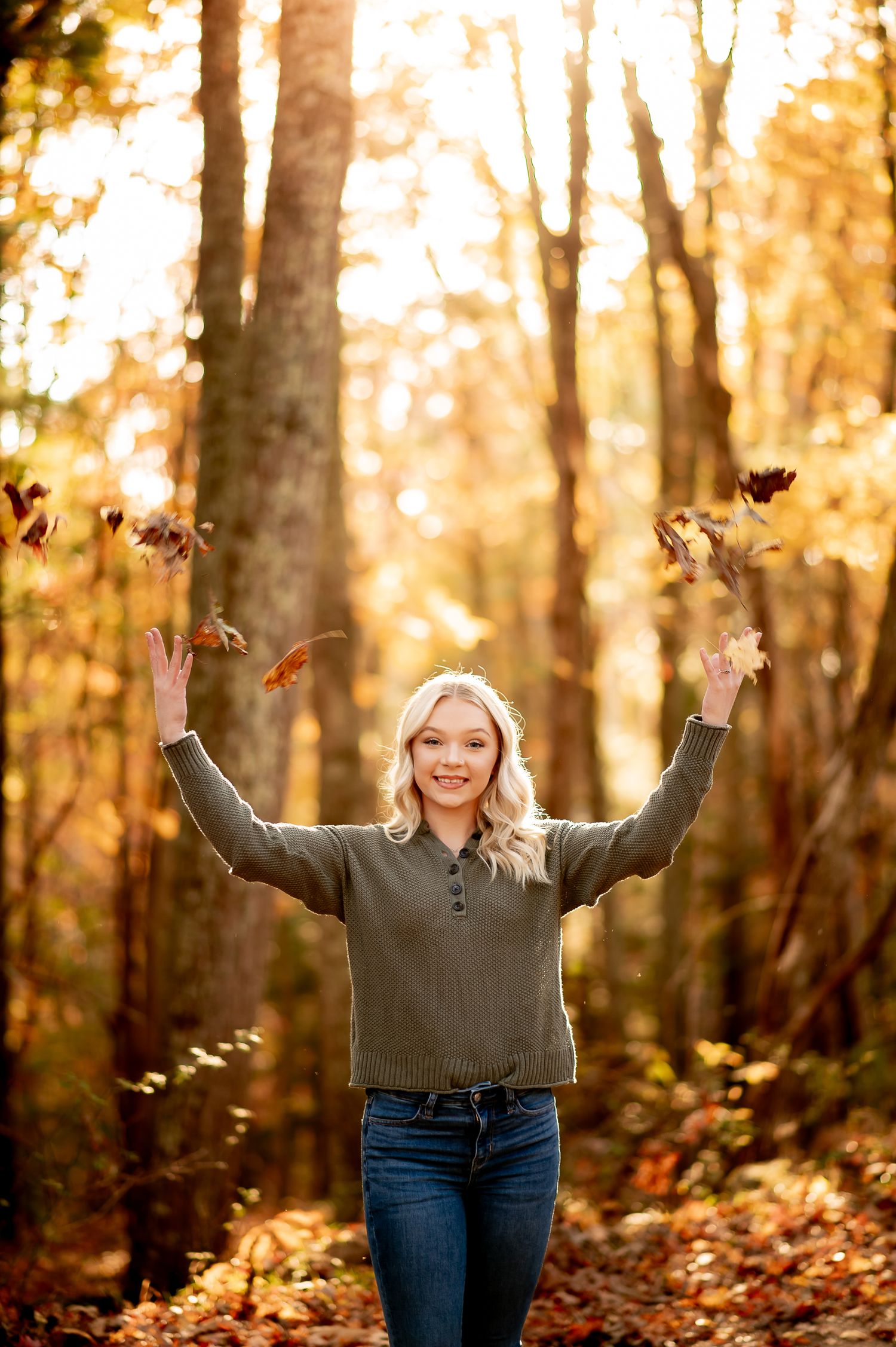 Person throwing autumn leaves in the air during golden hour forest photoshoot.