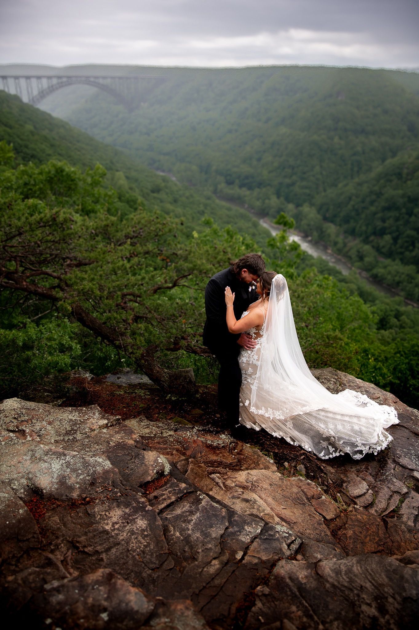 Wedding couple photographed along dramatic cliffside with sweeping valley views below.