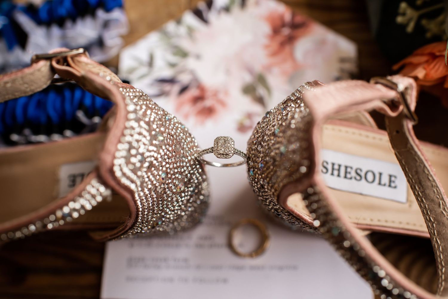Crystal-embellished rose gold bridal shoes with wedding rings displayed on paper.