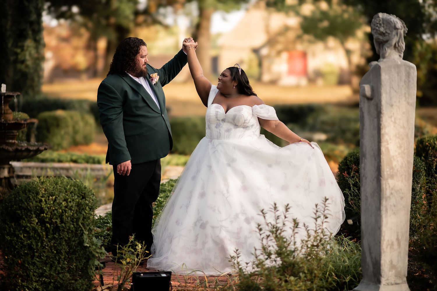 Bride in flowing white gown walking through a scenic outdoor garden setting.
