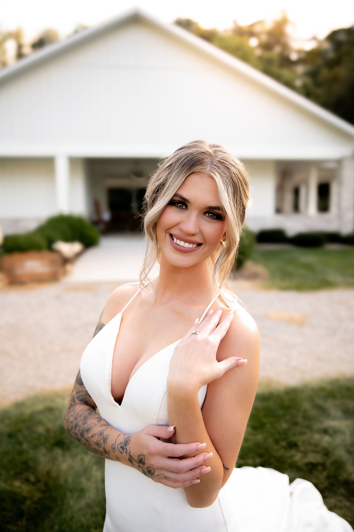 A person in a white dress poses outdoors near a white building in natural lighting.