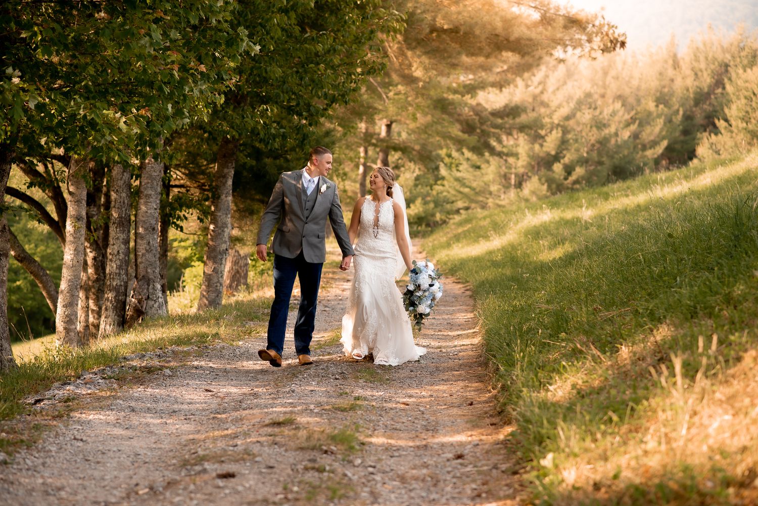 Wedding couple walking along a tree-lined path during golden hour.