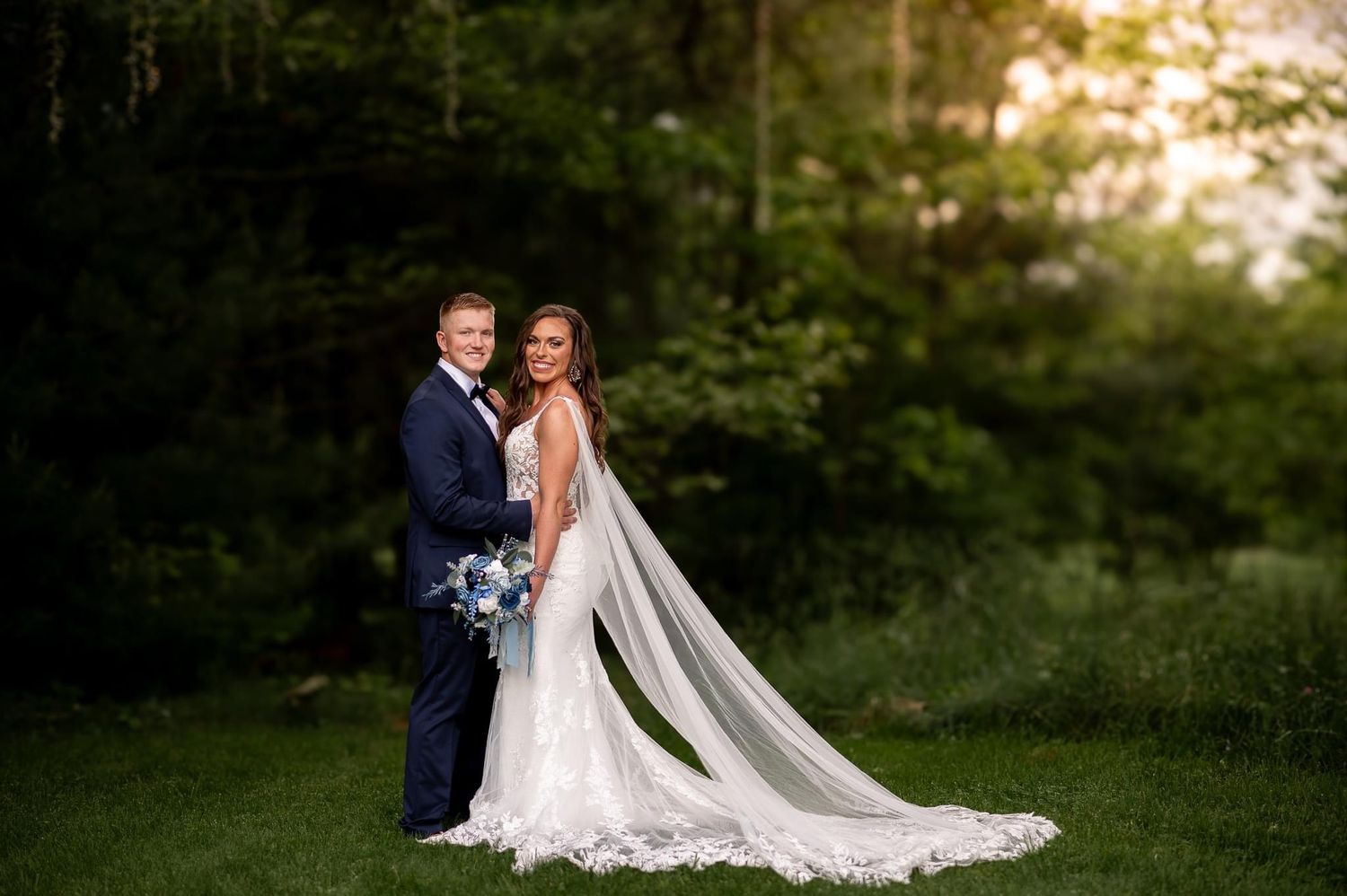 Elegant wedding portrait in forest setting with long flowing cathedral veil.