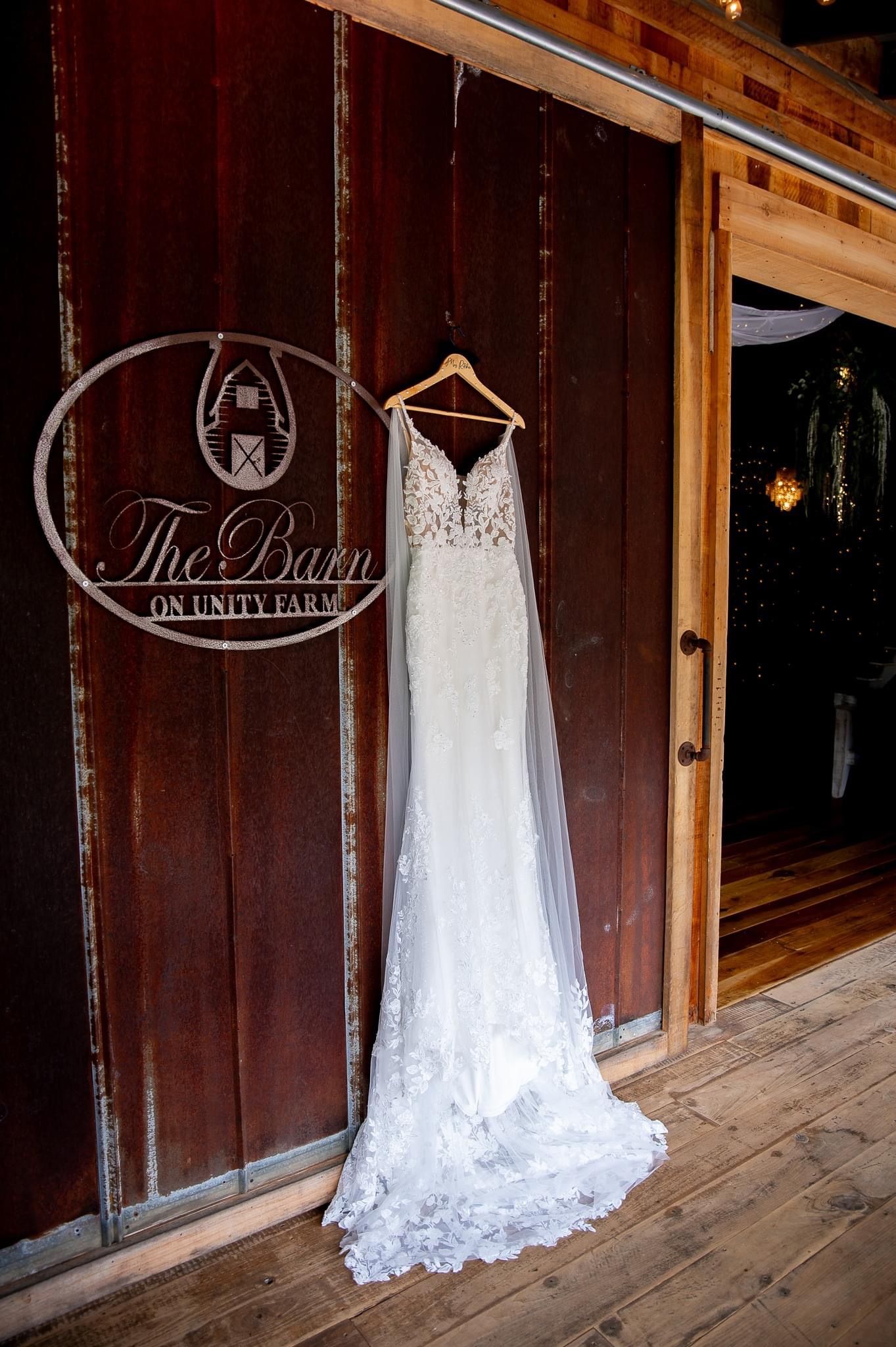Elegant white lace wedding dress hanging at The Barn on Unity Farm venue.