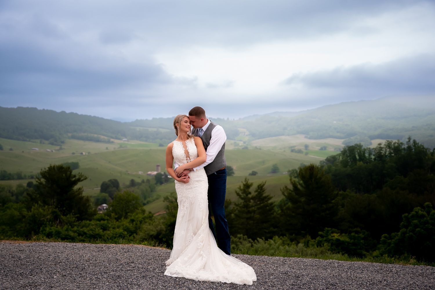 Newlyweds share an intimate moment against a mountainous landscape backdrop.