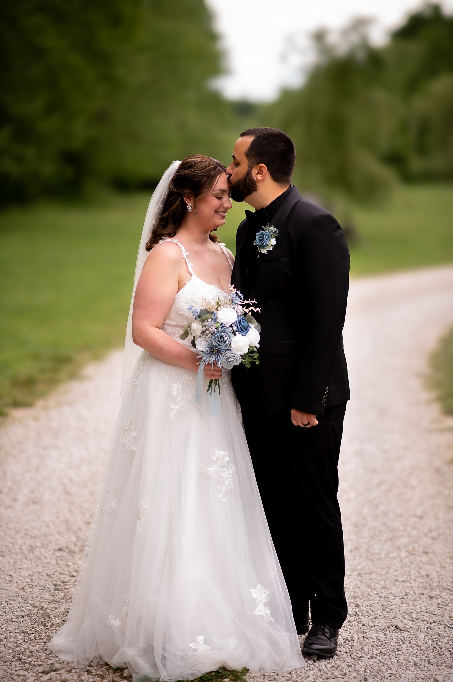 A bride and groom share tender moments on a gravel path surrounded by greenery.