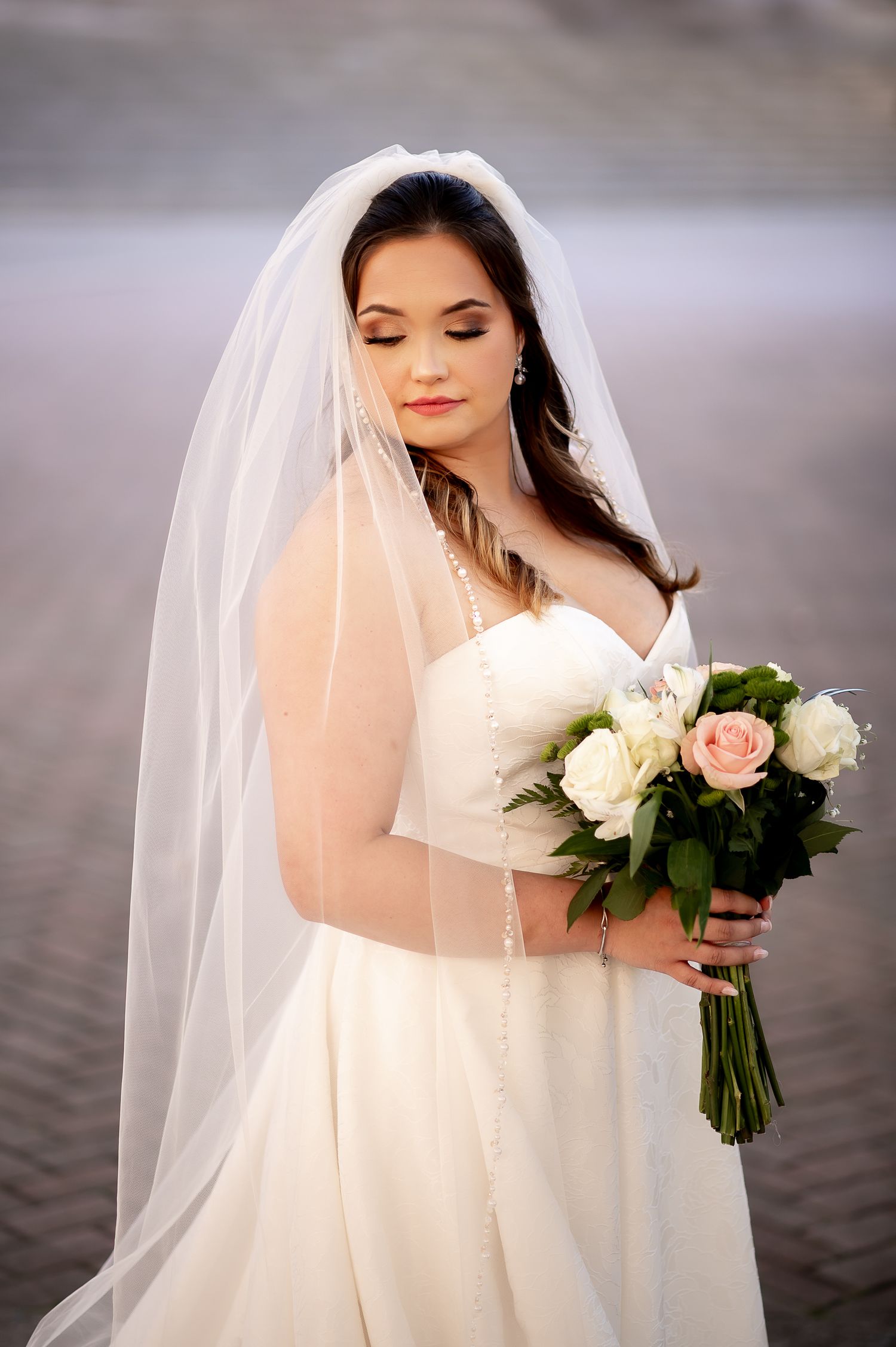 Bride in a classic white wedding gown holds a bouquet of roses against a misty background.
