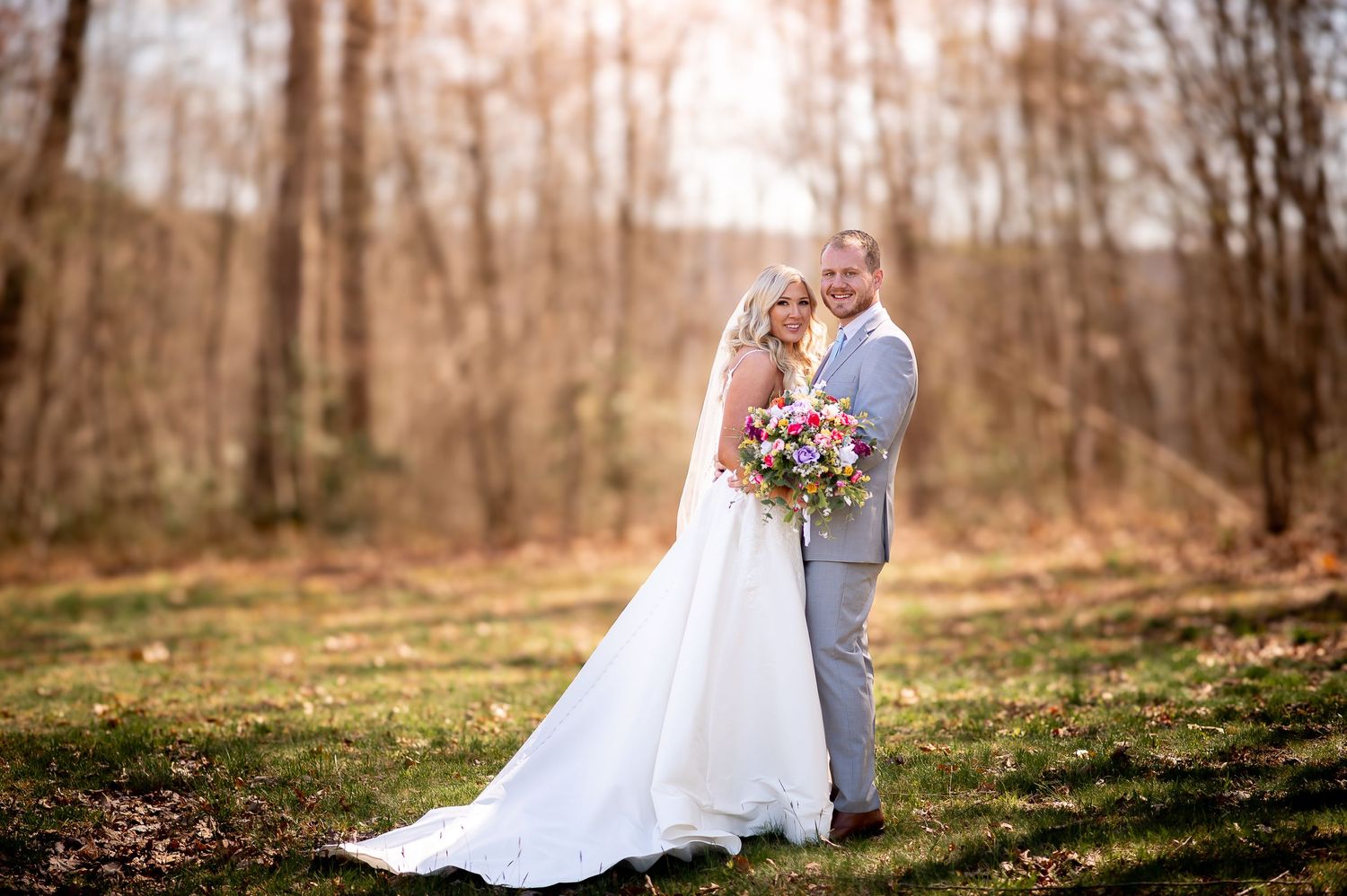 A wedding couple embraces in a serene forest setting with autumn foliage.