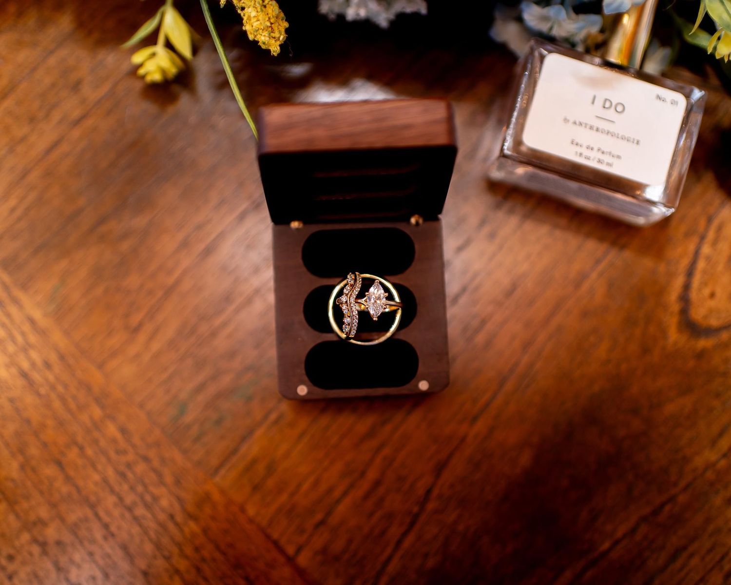 Wedding rings nestled in a dark wooden box on a rustic table surface.