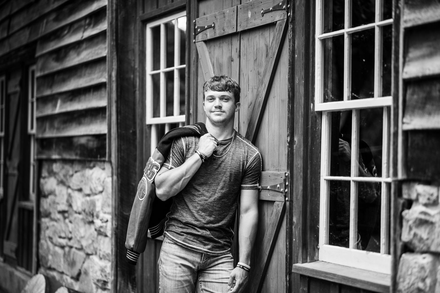 A black and white portrait against a rustic wooden building with stone foundation.