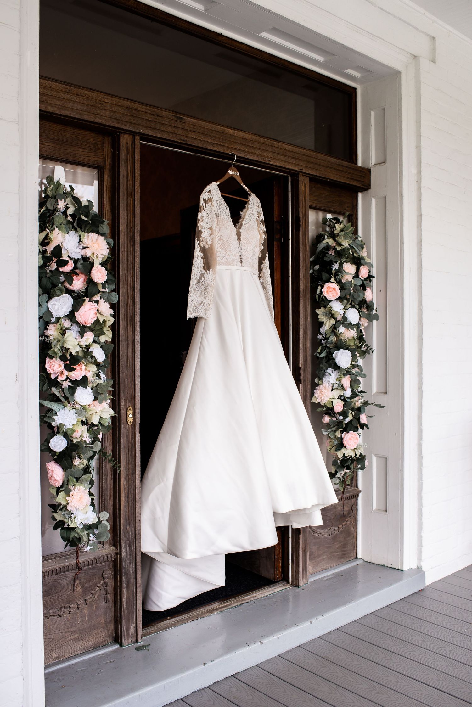 Wedding dresses displayed on hangers against white walls decorated with pink floral arrangements.