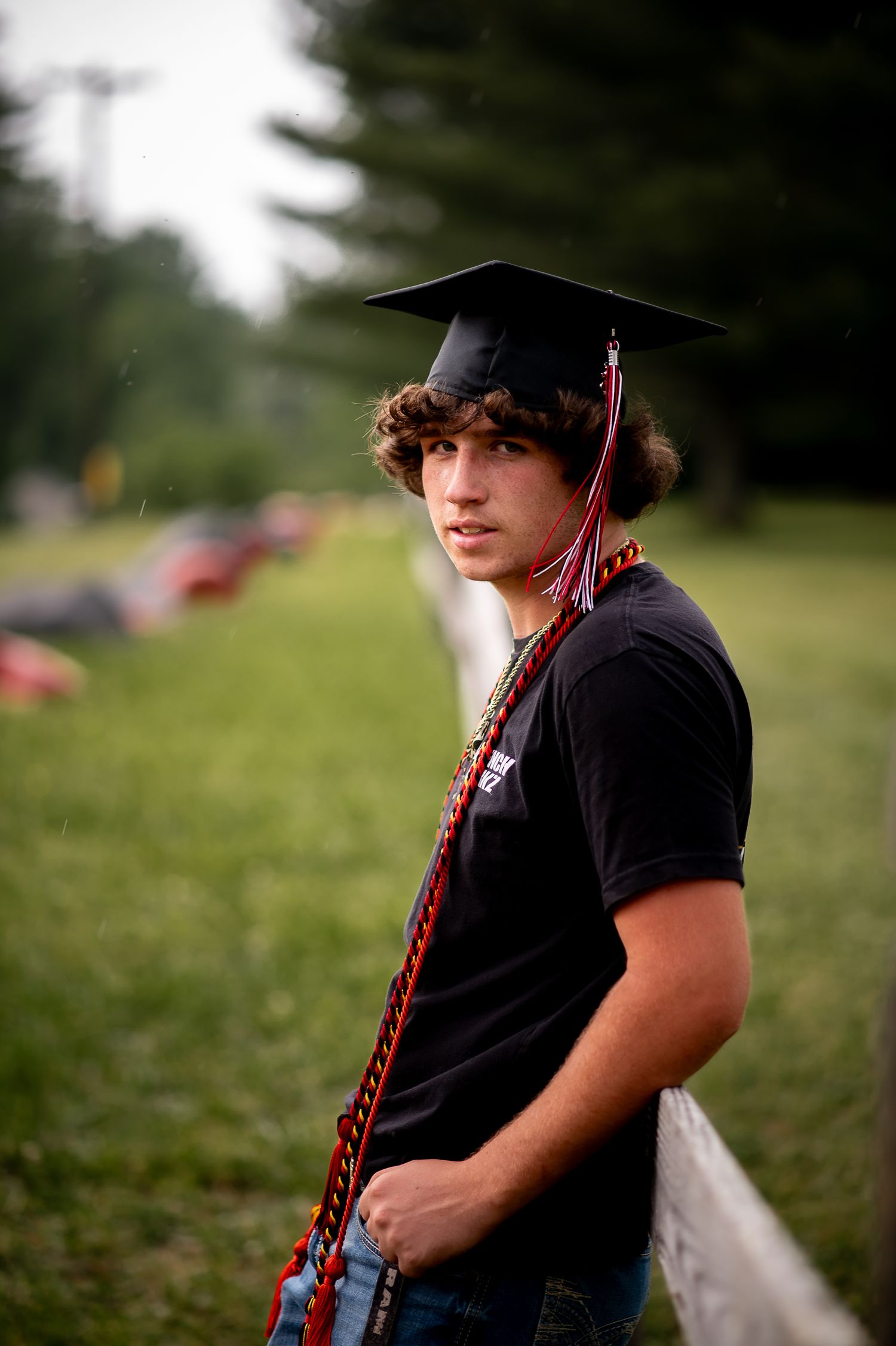 A graduation portrait of a graduate in black cap and gown against a blurred outdoor background.