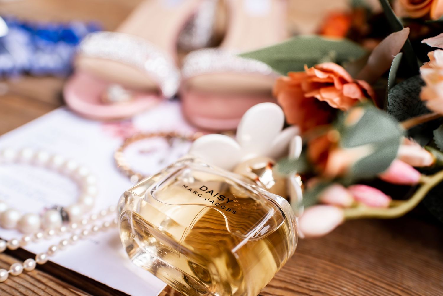 A elegant perfume bottle and wedding accessories arranged on a wooden surface with soft pink floral details.