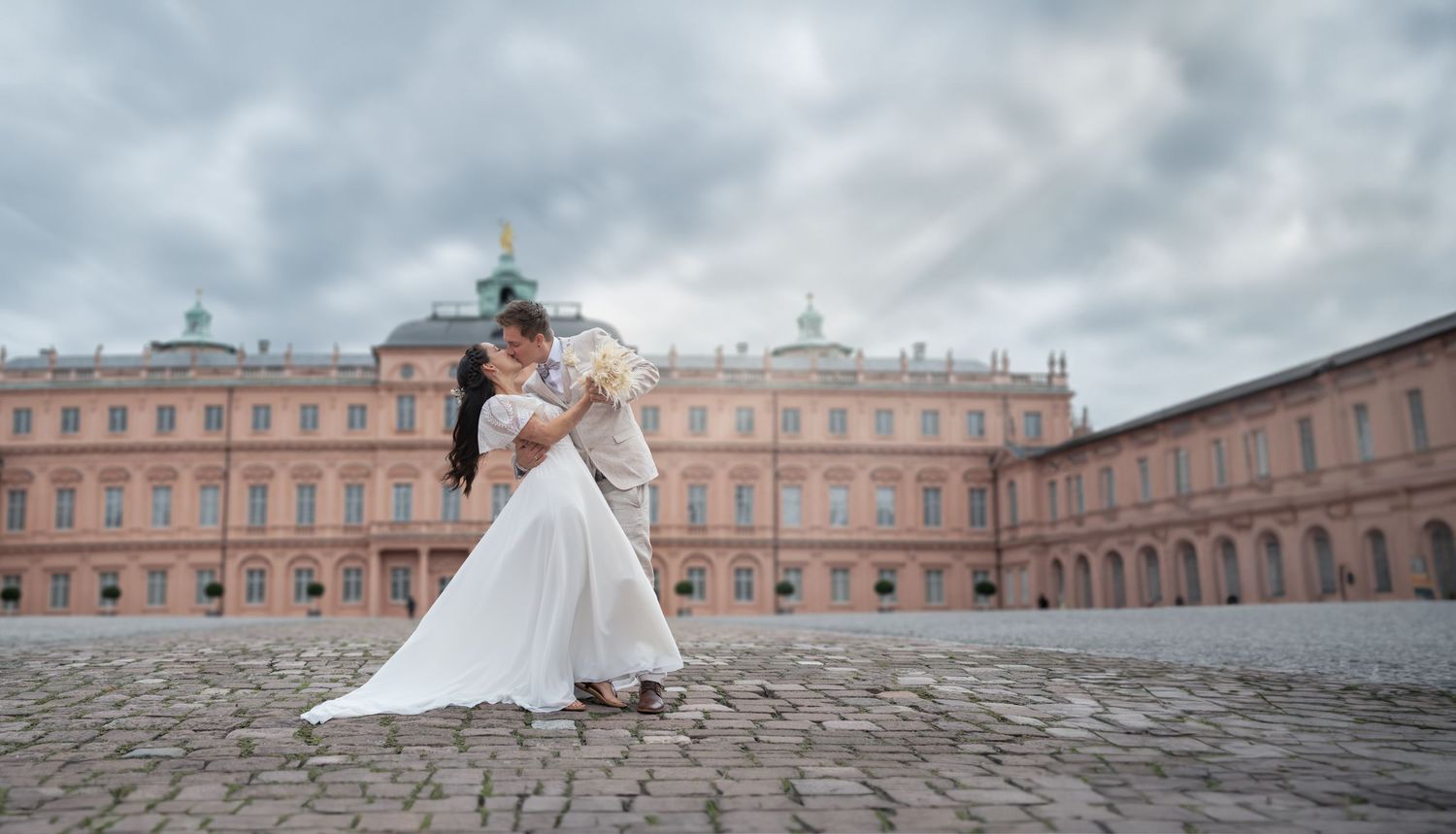 Foto des Brautpaares vor Schloss, mit Blumen in der Hand, lachen sich an