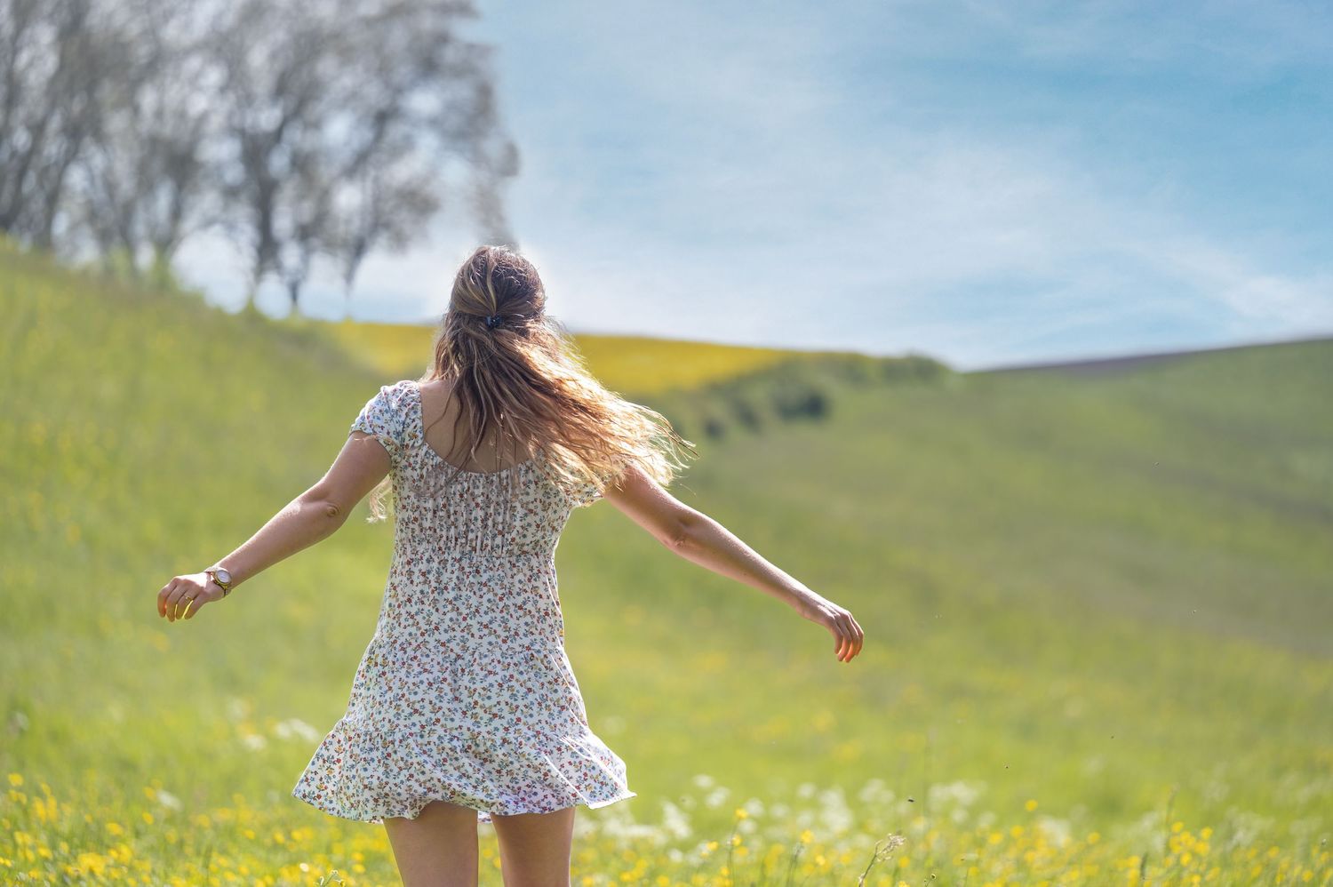 Frau in Sommerkleid von hinten tanzt auf Wiese