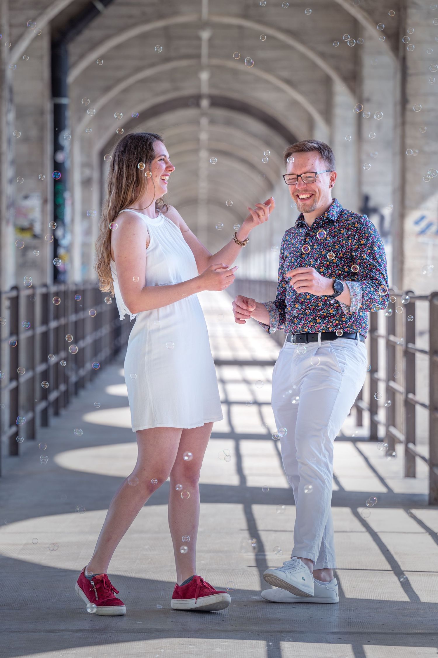 Fotografie einer Frau und Mann in schicken Klamotten, mit Seifenblasen, lachen