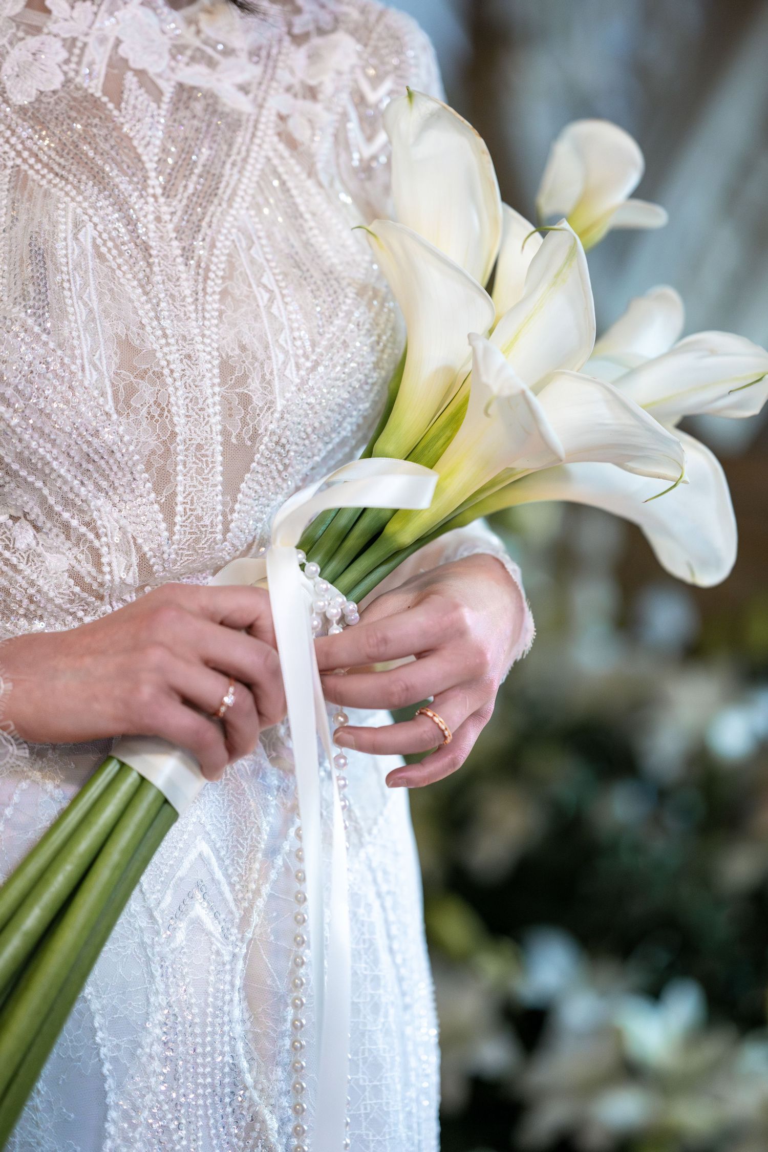 Detailaufnahme, Foto von einem Brautstrauß aus Lilien, Brautkleid und Hochzeitsrinde im Detail