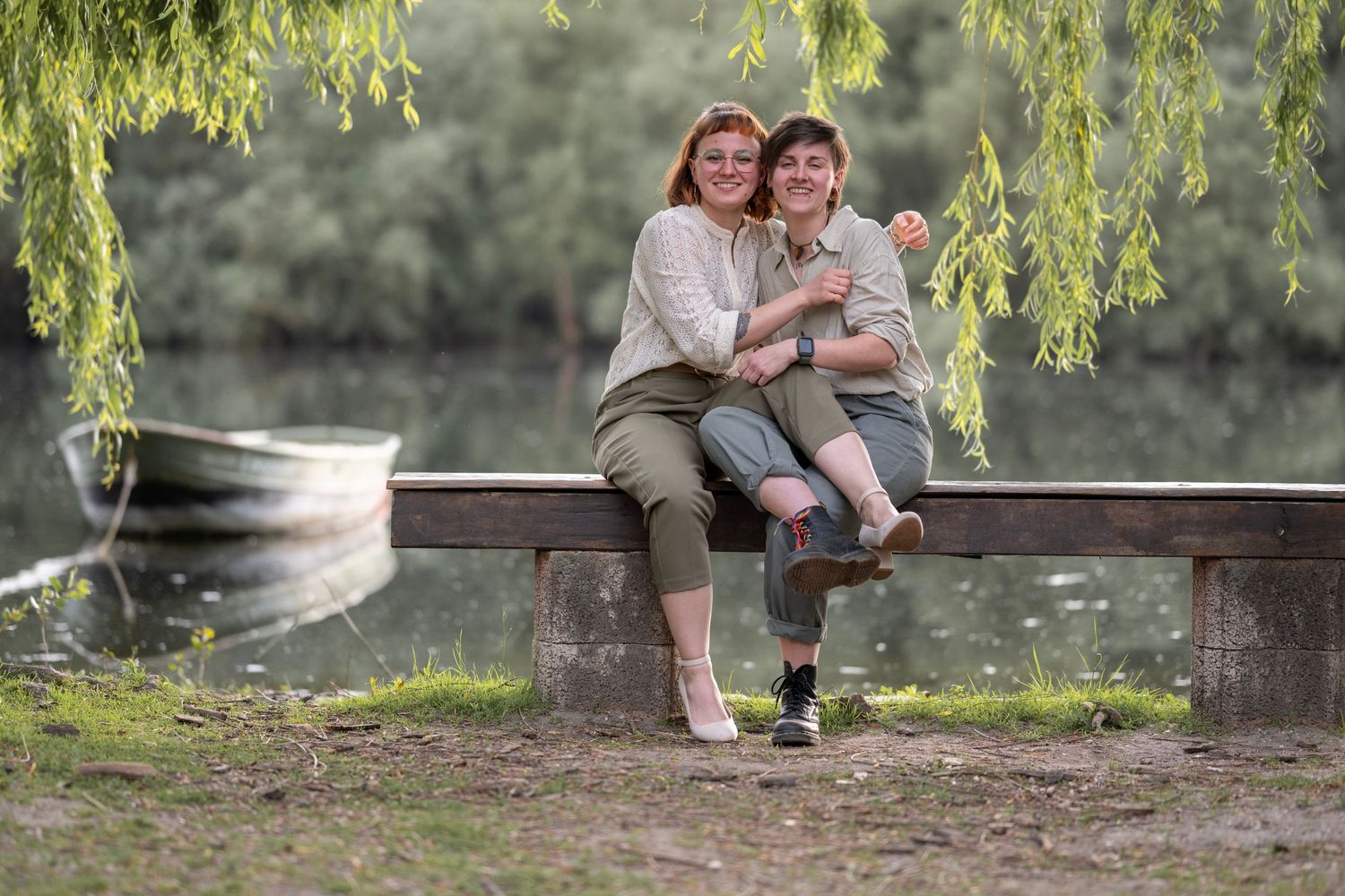 Foto von zwei Frauen die eng umschlungen auf einer Bank sitzen vor Wasser