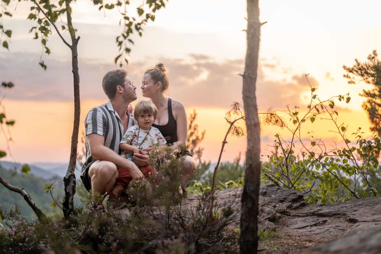 Eltern mit Kind auf einem Felsen bei Sonnenutergang