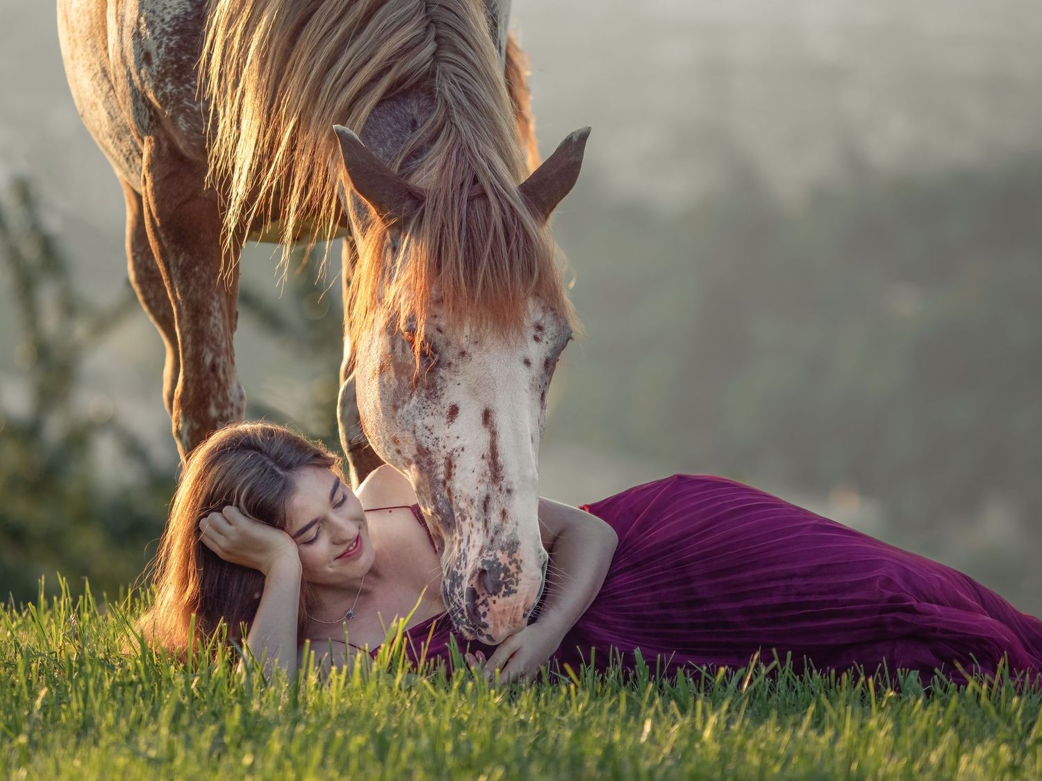 Frau liegt auf der Wiese mit einem Pferd