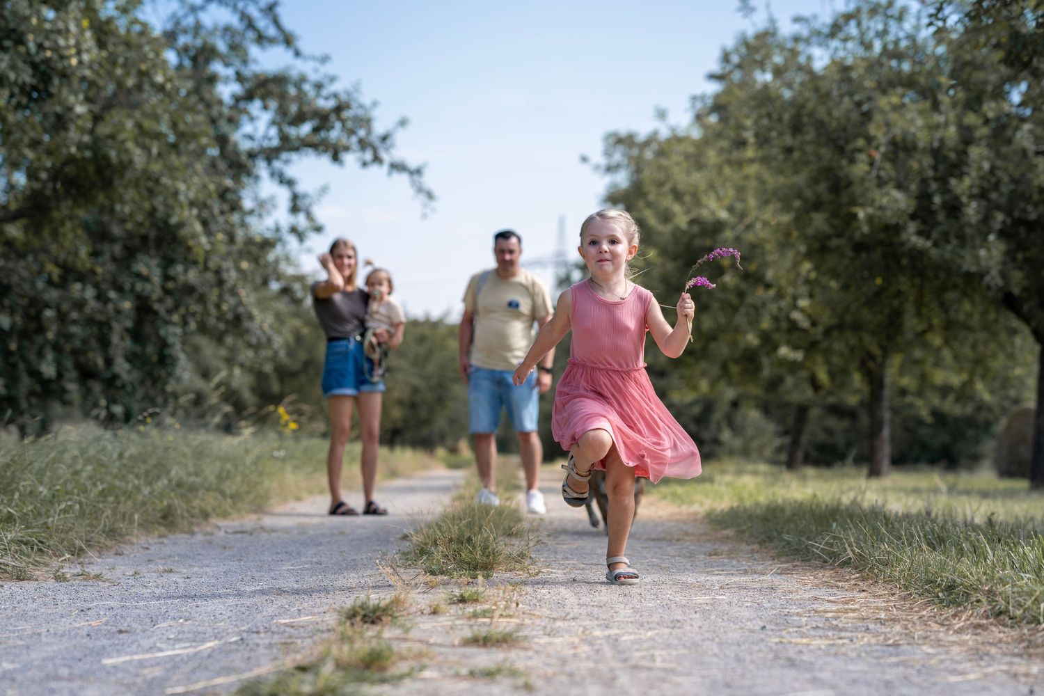 Eltern mit zwei Kindern laufen auf einem Feldweg. Ein Kind rennt auf die Kamera zu