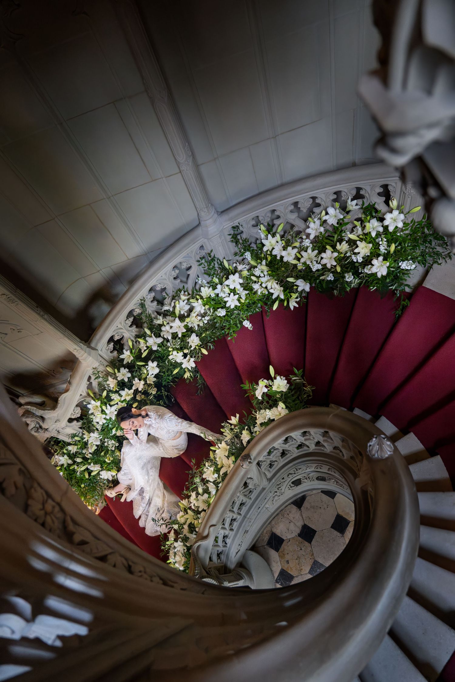 Braut sitzt auf einer Wendeltreppe, Sicht von oben, mit Blumen an der Treppe