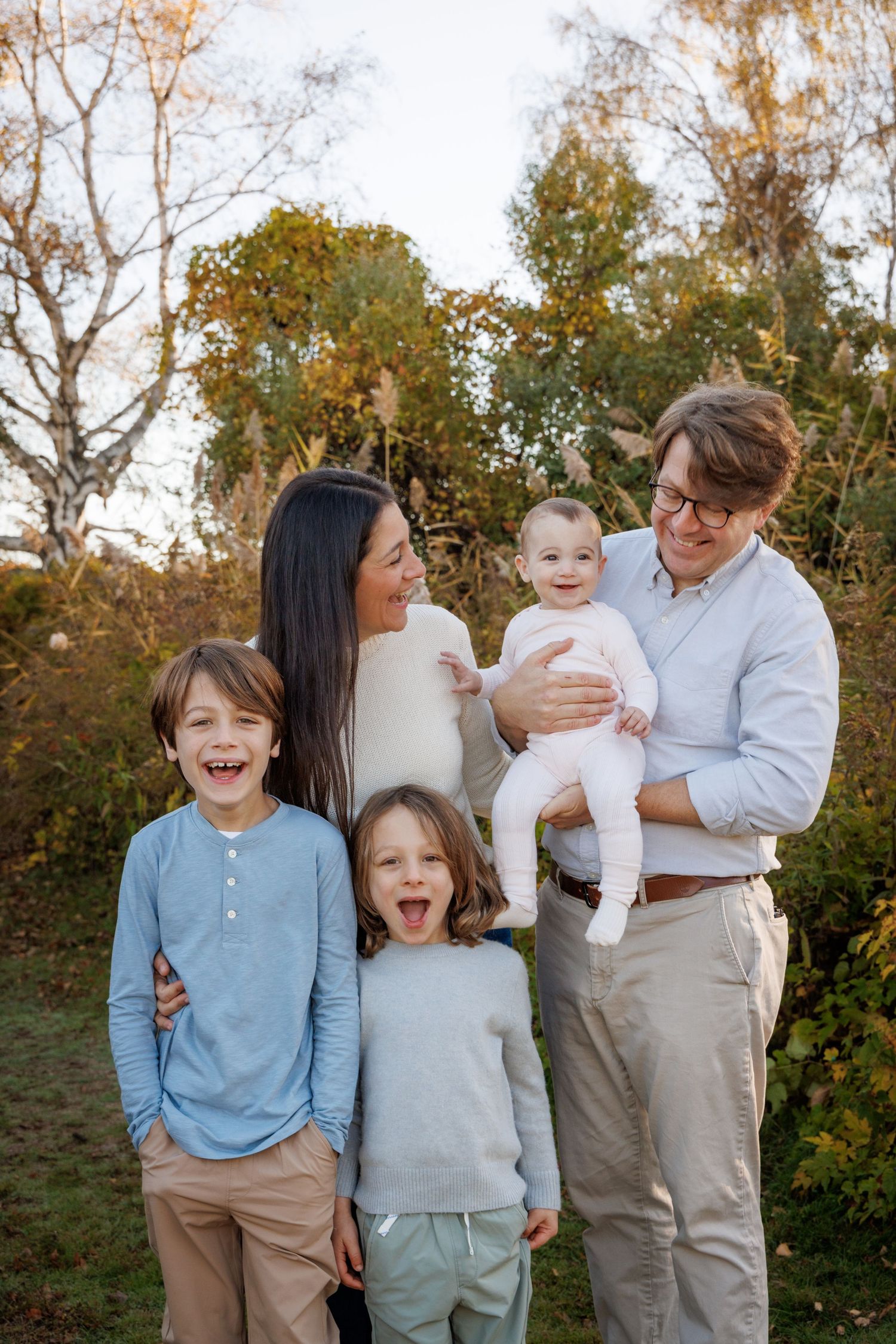 A joyful family photo session outdoors with casual coordinated outfits in blue and beige tones.