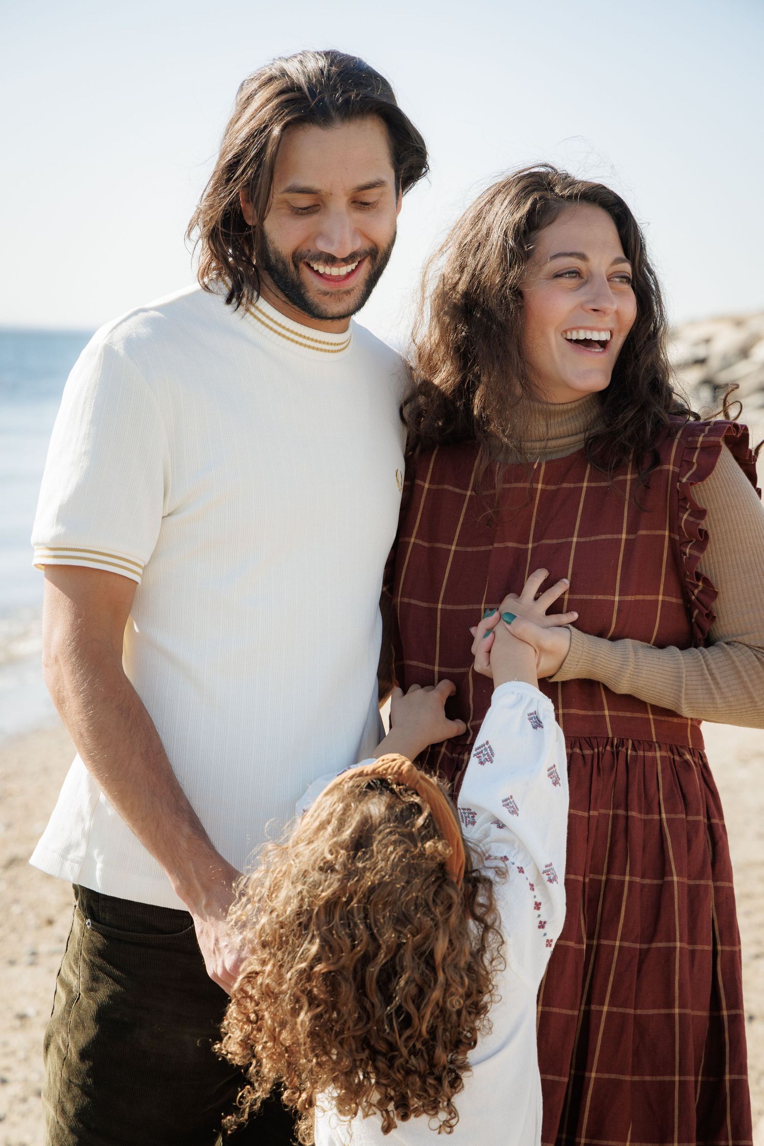 Candid beach family photos showing joyful laughter against sandy backdrop.