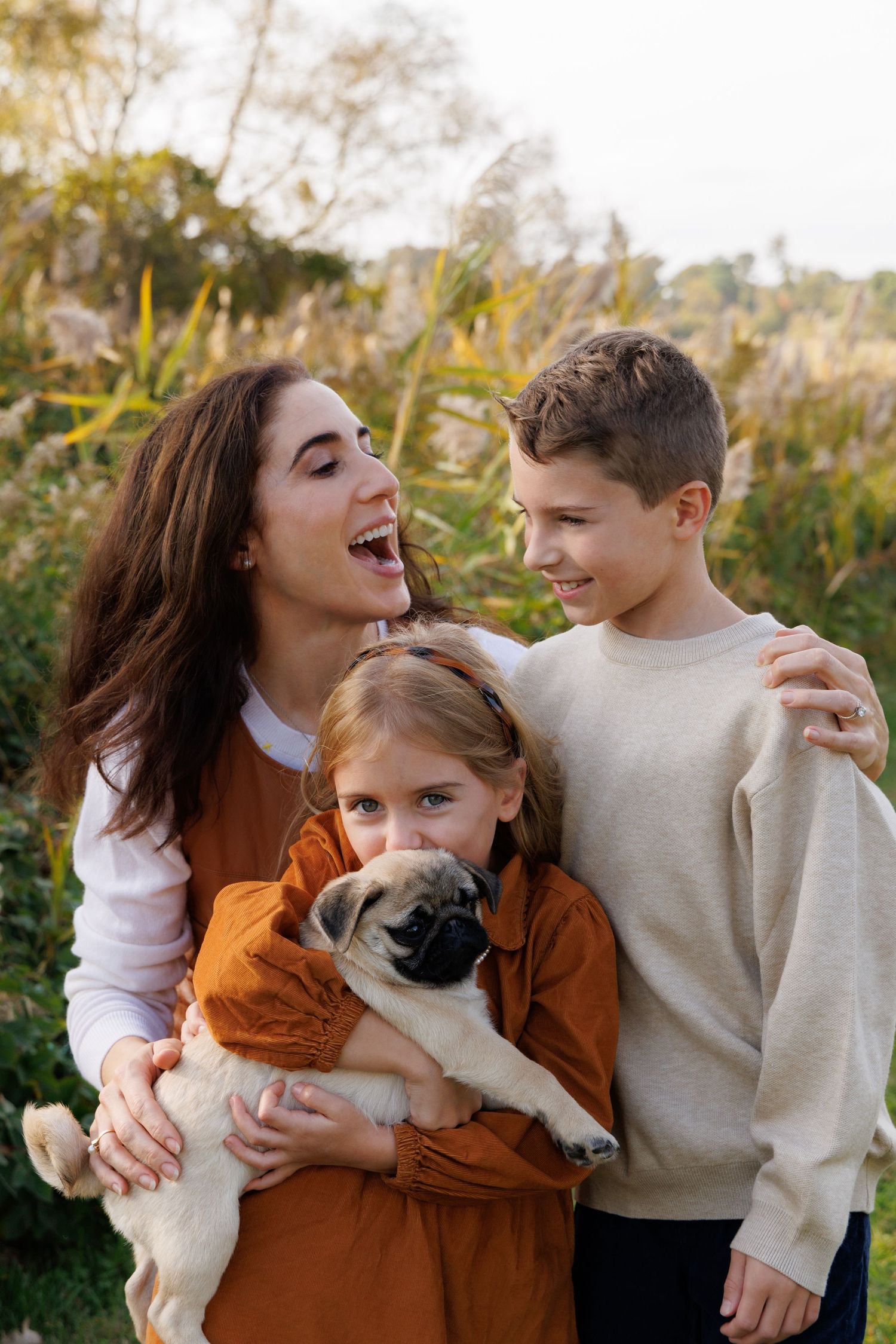 Playful family photos outdoors with a small white dog and autumn colors.