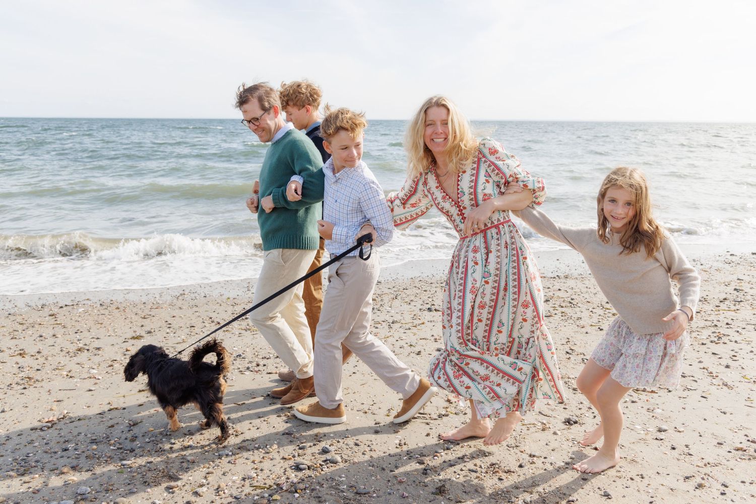Family playing and running together along a sunny beach shoreline.