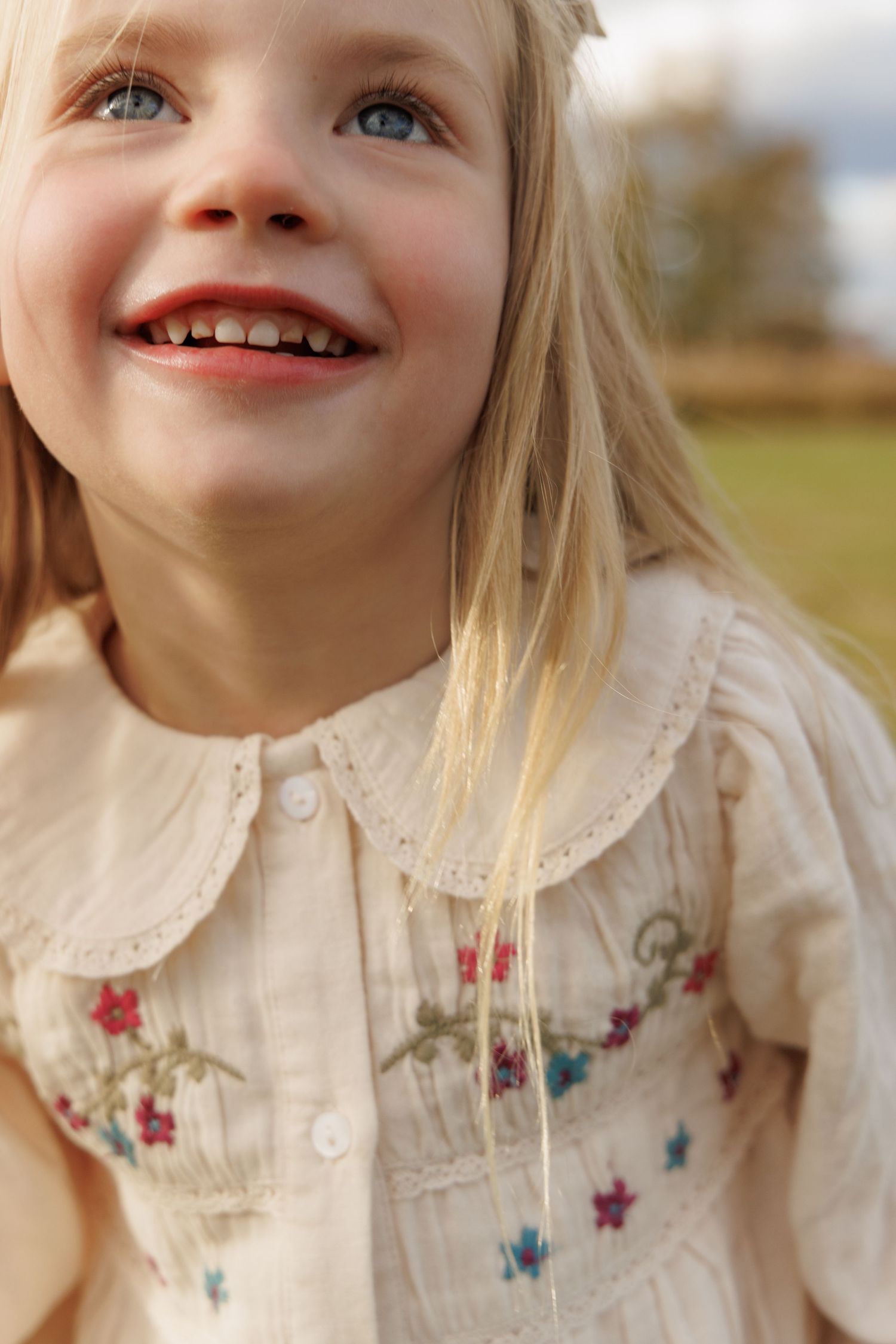 Close-up portrait showing delicate embroidered flowers on cream-colored clothing.