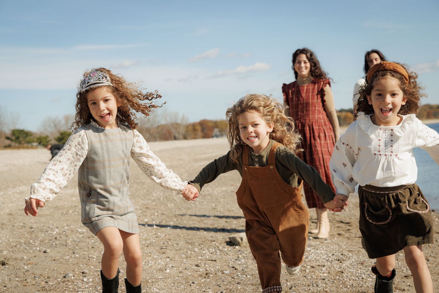Family running and playing together on a beach in casual autumn clothing.