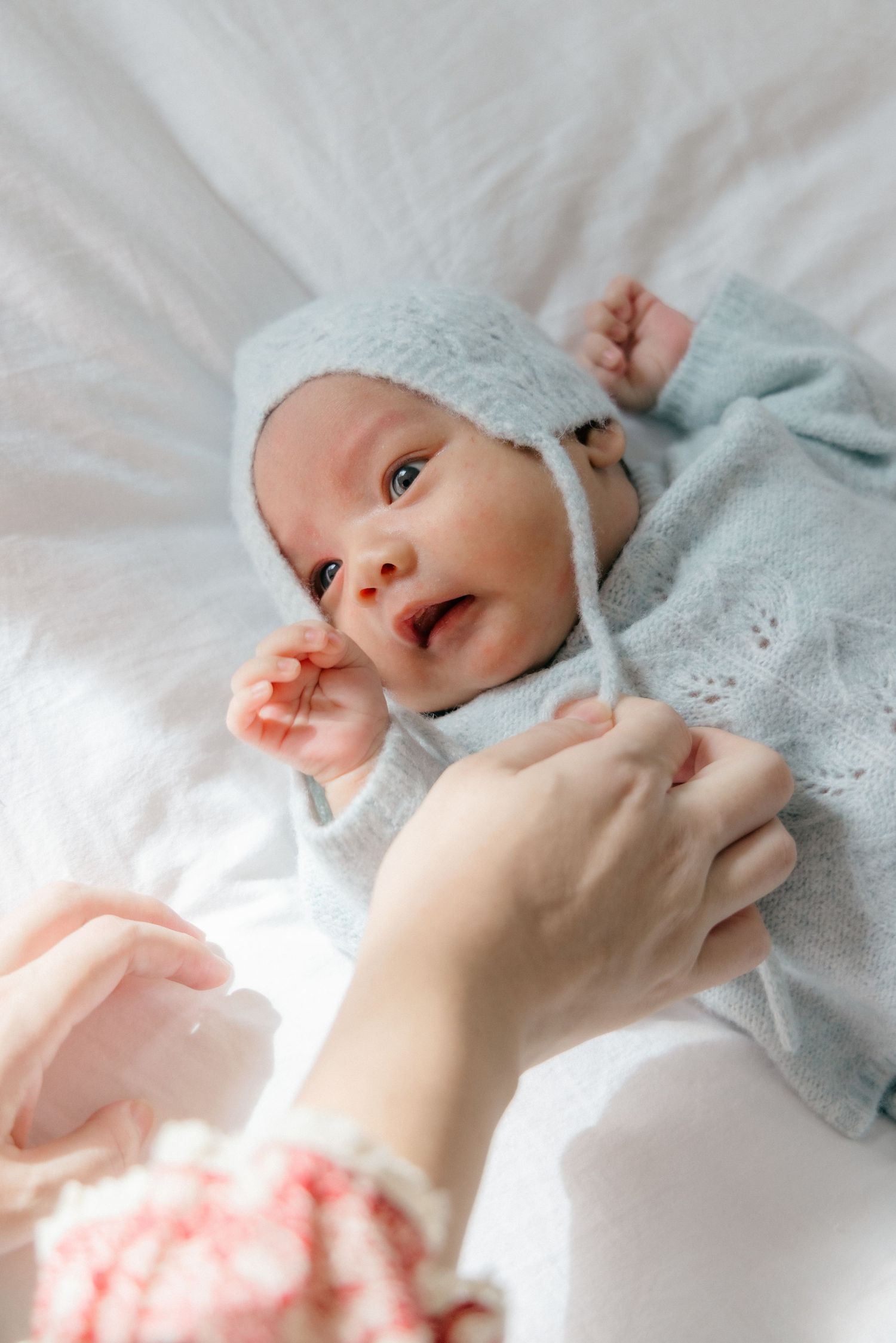 Newborn baby in soft blue blanket lying on white bedding.