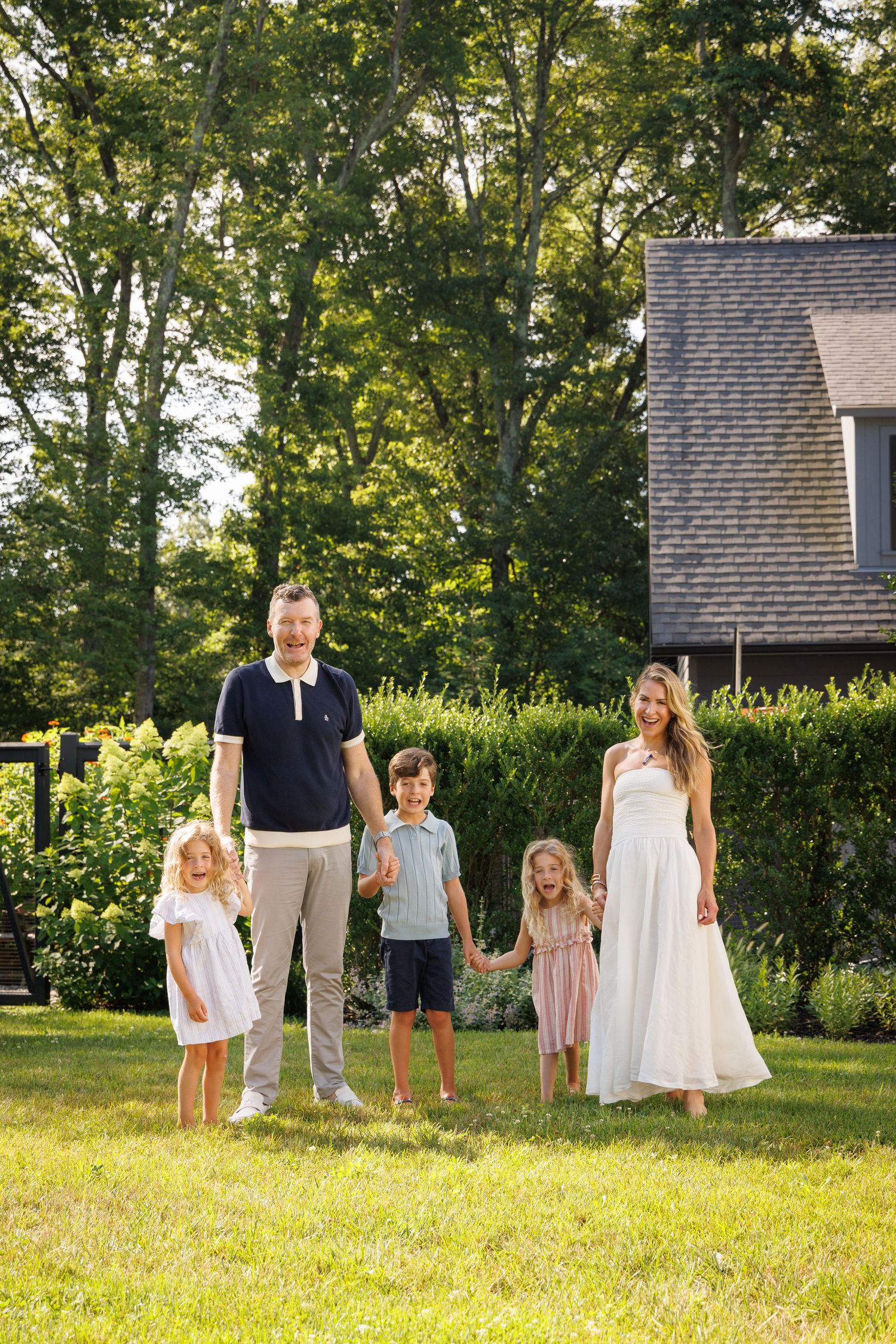Family portrait session in a sunny backyard with a house visible in the background.